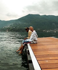 two people sitting on a dock in the water